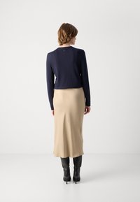 Mørkeblå genser med lange ermer, kombinert med et beige satengskjørt og svarte høye støvletter, sett fra baksiden.