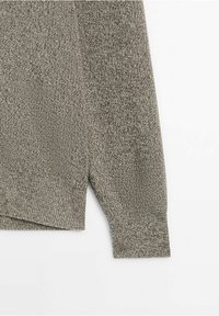 Gros plan sur la manche et l'ourlet d'un pull gris tricoté avec des poignets côtelés et un motif de point texturé sur fond blanc.