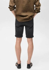 Schwarze Denim-Shorts mit umgeschlagenen Säumen, die mit einem braunen Langarmshirt kombiniert werden, was einen lässigen Schnitt und ein knielanges Design zeigt.