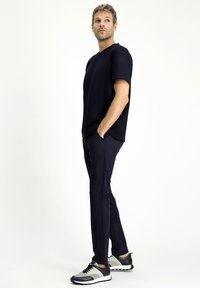 Camiseta de manga corta azul marino, pantalones negros ajustados y zapatillas deportivas grises y negras con cordones y suela de goma; textura de tela suave.