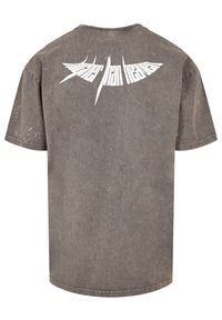 Šedé oversized tričko vyrobené z bavlny s žebrovaným výstřihem. Na zadní straně se nachází bílý grafický text, který zobrazuje stylistické písmo.