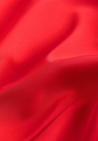 Jasně červená tkanina s hladkou, saténově podobnou texturou, zobrazující jemné záhyby a odlesky, které ukazují živou barvu a lesk.