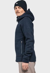 Marineblauer Hoodie aus strukturiertem Gewebe, mit verstellbarem Kordelzug und seitlichem Reißverschlussfach. Rippbündchen und -saum sorgen für zusätzlichen Komfort.