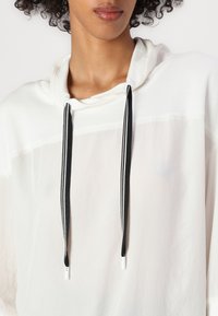 Weißer Hoodie mit schwarzen Kordeln, lässiger Schnitt, gerippter Kragen und leichtem, halbtransparentem Material. Keine sichtbaren Muster oder Akzente.