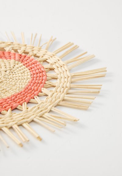 Rund vevd matte laget av naturlige fibre. Har en sentral kremfarget sirkel med en korallfarget kant og utstående strå-lignende detaljer rundt kanten.