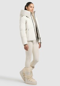 Giacca a puffo bianca con un alto collare, chiusura con zip e due tasche laterali, abbinata a pantaloni aderenti coordinati e stivali invernali.