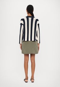 Pruhovaný pletený cardigan v námořnické modři a krémové barvě s otevřeným zadním dílem. Kombinován se zelenou prošívanou sukní s hladkou texturou a přiléhavým střihem.