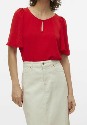 Rote kurzärmlige Bluse mit rundem Halsausschnitt und Schlüsselloch-Detail, kombiniert mit einem cremefarbigen Jeansrock mit Fronttaschen.