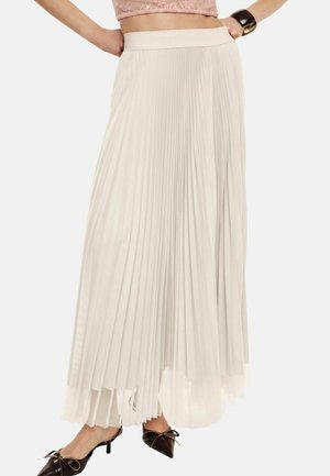 Donna che indossa una gonna lunga plissettata color crema a vita alta abbinata a décolleté nere con punta appuntita e fiocchi.