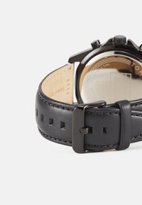 Bracelet de montre en cuir noir avec boucle réglable, présentant une finition lisse et des coutures décoratives, mettant en avant un design épuré et une durabilité.