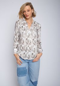 Leichte, gemusterte Bluse mit einem Kettenmuster in Beige und Weiß, ausgestattet mit einem kragenlosen Ausschnitt und gestreiften Manschetten, kombiniert mit Patchwork-Jeans.