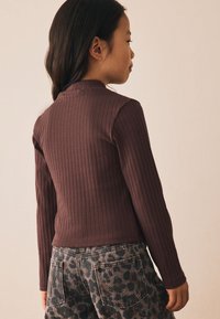 Top de manga larga acanalado en marrón oscuro, con un cuello alto. Combinado con jeans grises con un patrón de leopardo negro.