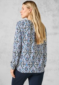 Musterbluse mit einem Diamantdesign in Blau-, Schwarz- und lila Tönen. Hergestellt aus leichtem Stoff, mit langen Ärmeln und entspanntem Schnitt.