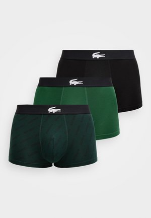 Trys vyriški bokseriai: juodos spalvos, tamsiai žalios su Lacoste logotipais ir vientisos žalios spalvos, kiekvienas su juodu juosmeniu, kuriame yra baltas krokodilo logotipas.