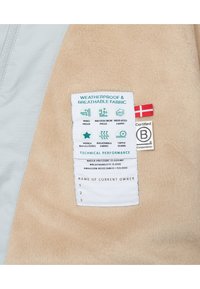 Tessuto in pile beige con un bordo grigio chiaro, dotato di un'etichetta che mostra le istruzioni per la cura e icone relative alle prestazioni tecniche.