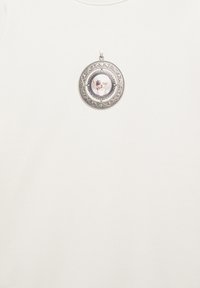 Stříbrný kulatý medailon s propracovanými vzory, uvnitř s malou fotografií psa s velkýma ušima.