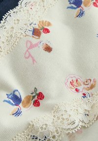 Kremowa tkanina z niebieskimi i brązowymi czajnikami, czerwonymi truskawkami, rogalikami i kremową koronką wzdłuż krawędzi.