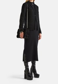 Černý texturovaný blazer s dvěma knoflíky, spárovaný s černou žebrovanou sukni se bočními rozparky. Dokončeno lesklými černými platformovými botami a koženou kabelkou s kožešinou.