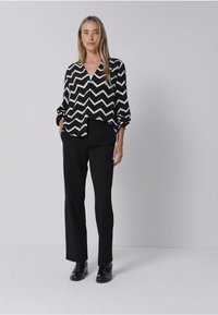 Blusa a zigzag bianco e nero abbinata a pantaloni neri su misura e scarpe nere, che mette in mostra una vestibilità rilassata e maniche lunghe.