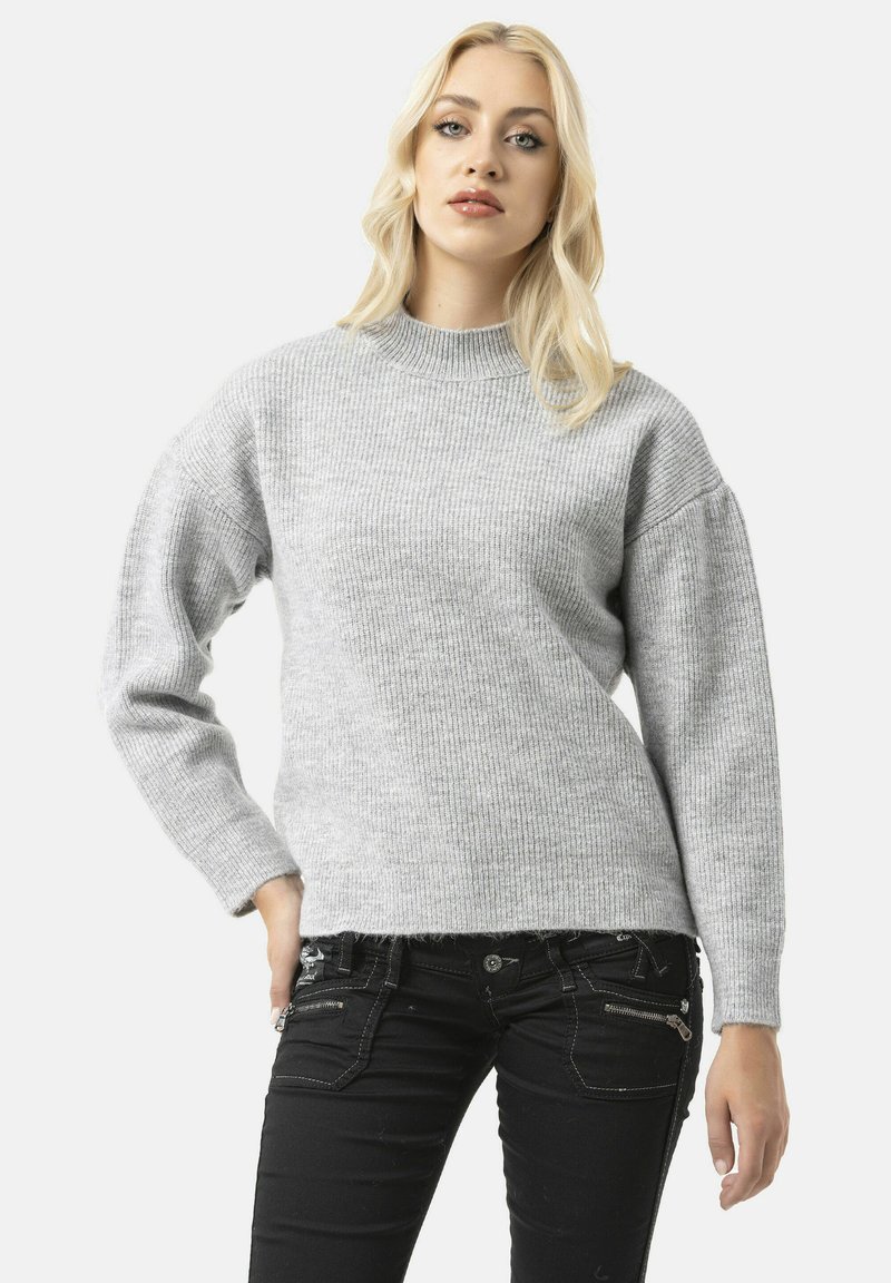 Grijze geribbelde trui met een hoge halslijn en verlaagde schouders. Gecombineerd met zwarte jeans met ritssluitingen en een aansluitend ontwerp.