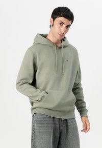 Hooded sweatshirt in muted green cotton blend, featuring a front pocket, ribbed cuffs, and a small logo accent on the chest.