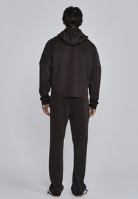 Bruine hoodie met een cropped zoom, gecombineerd met bijpassende broek. Gladde stof, relaxte pasvorm en minimale naden zichtbaar.