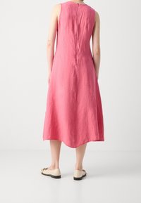 Ärmelloses pinkes Leinenkleid mit A-Linien-Form, ausgestattet mit einem Reißverschluss am Rückenausschnitt und einem geschwungenen Saum. Kombiniert mit hellen Ballerinas.