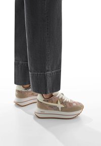 Die Turnschuhe haben ein oberes Material aus leicht rosa Netzstoff mit beigen Wildlederelementen und einem weißen Schnürsystem. Dicke weiße Sohlen mit einer strukturierten braunen Außensohle.
