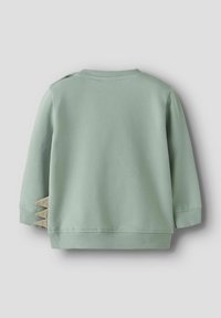 Sudadera verde de algodón con mangas largas, puños acanalados y un acento único beige que asemeja garras en el lado inferior izquierdo.