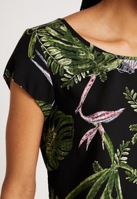 Blusa negra con estampado botánico de hojas verdes y acentos rosas. Mangas cortas, escote redondeado y textura de tela suave.