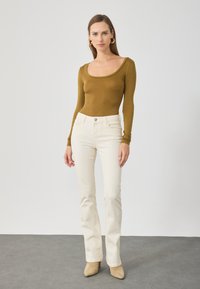 Bodysuit de manga longa em verde-oliva, combinado com jeans flare creme e saltos bege. Design simples, textura canelada e silhueta ajustada.