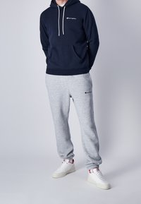 Sudadera de marineros con cordones y bolsillo delantero, combinada con pantalones de chándal gris claro. Zapatillas blancas con acentos rojos completan el conjunto.