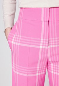 Pantalons à carreaux roses avec une texture lisse, présentant des rayures blanches et une poche latérale. La taille est unie rose, en harmonie avec le motif.