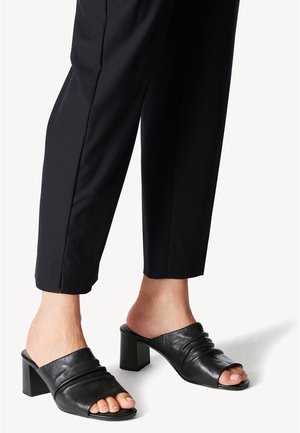 Černé kožené sandály s otevřenou špičkou, se sešitou horní částí a čtveratým blokovým podpatkem. Nosené s kalhotami ke kotníkům v černé barvě.