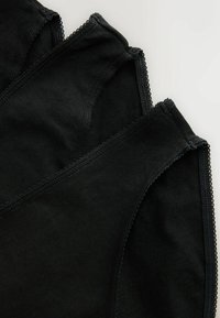 Three black cotton underwear briefs layered with visible stitching and scalloped edges on a white surface.