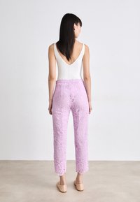 Lace roze broek met een golvende zoom, voorzien van bloemenpatronen en een relaxte pasvorm, gecombineerd met een witte geribbelde body.