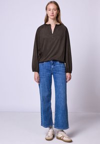 Mørkebrune langærmede top med en kvart lynlås, parret med brede blå denimjeans og beige sneakers. Simple, afslappet pasform.