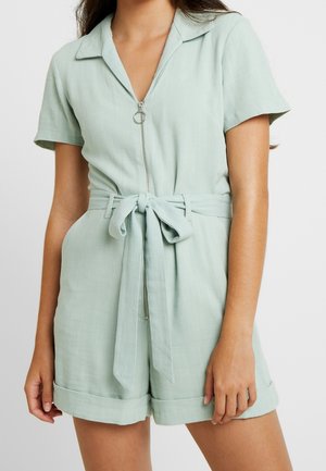 Mintunvihreä lyhyt haalari, jossa on etuvetoketju, kaulus, lyhyet hihat ja solmittava vyötärönauha. Ominaisuuksiin kuuluvat käännetyt hihansuut ja kevyt kangas.