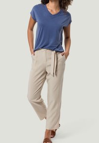 T-shirt bleu à col en V avec des manches courtes, associé à un pantalon beige taille haute avec une ceinture à nouer et des poches latérales. Des sandales marron viennent compléter le look.