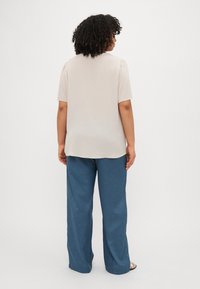 Beige kortermet bluse med en lett glans og rund kant, kombinert med løse blå bukser laget av et teksturert stoff.