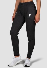 Dark gray athletic pants with a fitted design, featuring a white logo, side zip pockets, and tapered ankles. Smooth texture with stretch.