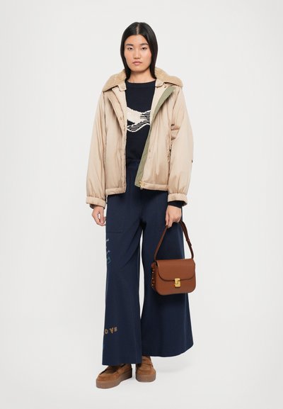 Doudoune beige clair avec un col en fourrure, pull marine avec un motif graphique, pantalon navy à large jambe, et sac à bandoulière marron avec des détails en or.