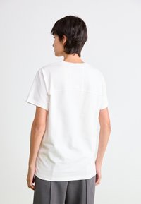Hvid bomulds t-shirt med en afslappet pasform, korte ærmer og en subtil sømdetalje på ryggen, parret med grå bukser.