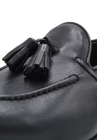 Black leather loafers featuring decorative tassels, smooth texture, stitched detailing along the edges, and a rounded toe design.