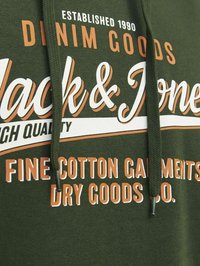 Sudadera de color verde oscuro con cordón, que presenta un gran texto en blanco y naranja. El diseño incluye la marca y detalles sobre la calidad del tejido.