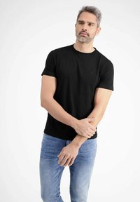 Black short-sleeve t-shirt with a round neck, made of cotton, featuring a subtle logo detail on the chest, paired with light blue denim jeans.