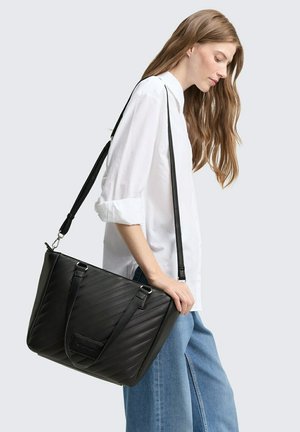 Sac fourre-tout noir matelassé avec deux sangles ajustables. Caractérisé par une forme structurée et une petite poche avant. Matériau synthétique lisse.