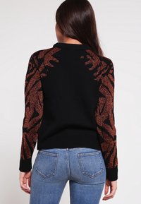 Svart tröja med texturerade, metalliska bronzfärgade mönstrade ärmar, med rund halsringning och ribbade muddar och fåll. Tajt passform.