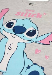 T-shirt en coton gris avec un personnage de dessin animé bleu aux grands yeux et des accents roses, entouré de petits coeurs roses.