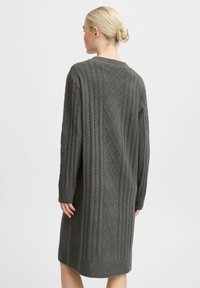Gestricktes graues Sweaterkleid mit einem strukturierten Rautenmuster, gerippten Bündchen und lockerer Passform, das bis zur Oberschenkelmitte reicht, von hinten betrachtet.